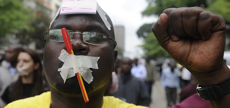A man with tape over his mouth raises his fist in protest